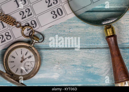 Kalender, Lupe und Antik Silber Taschenuhr alte blaue Holz Tisch Stockfoto