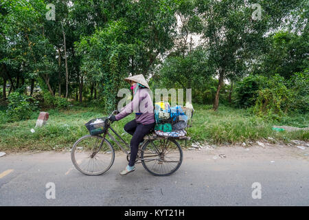 Straßenansicht im ländlichen Saigon (Ho Chi Minh City), Südvietnam: Lokale vietnamesische Frau mit einem konischen Hut auf dem Fahrrad einer altmodischen Frau Stockfoto