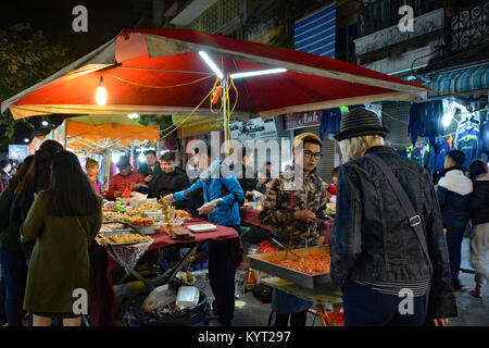 Hanoi, Vietnam - 15. Dezember 2017. Ein junger Mann bedient Kunden in einer Nacht Marktstand mit regionalen Lebensmitteln in der historischen Altstadt von Hanoi Stockfoto