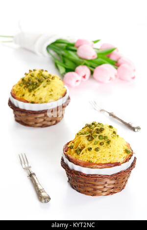 Timbale mit tagliolini Nudeln, Erbsen und Schinken in Keramik Aufläufe auf weißen Tisch mit rosa Tulpen. Weißer Hintergrund, Frühling Essen. Stockfoto