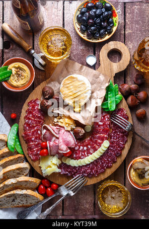 Mix aus verschiedenen Snacks und Vorspeisen: Wurst, Brot, Oliven, Käse, Kastanien, Erbsen und Bier auf Holzbrett. Ansicht von oben Stockfoto