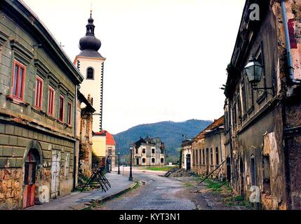 Die kroatische Stadt Hrvatska Kostajnica ist im Una River an der Grenze zu Bosnien-herzegowina. Kurz nach Beginn der jugoslawischen Kriege die Stadt Teil der Republik Serbische Krajina wurde bis 1995, als es durch kroatische Truppen zurückerobert. Die Innenstadt wurde schwer beschädigt und die katholische Kirchen wurden zerstört. Das Bild zeigt die zerstörte Davor Trstenjak-Street und die rekonstruierte Katholische Kirche sieben Jahre nach dem Krieg, im November 2002. Stockfoto