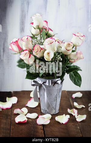 Schönen Blumenstrauß aus roten und weißen Rosen mit Baby's Atem in einem Metall Landhausstil Vase von gefallenen Blütenblätter umgeben. Stockfoto