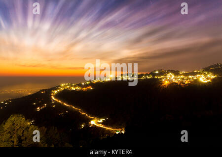 Wolken ziehen schnell bei einem schönen Sonnenuntergang in Mcleod Ganj, Dharamsala, Himachal Pradesh, Indien. Leichte Spuren von Fahrzeugen klettern auf den Berg Stockfoto