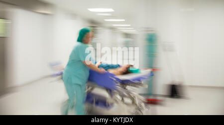 Motion verschwommenes Bild von einer Krankenschwester in Eile Wurf nach unten schieben eine sterile Licht Krankenhaus Flur. Stockfoto