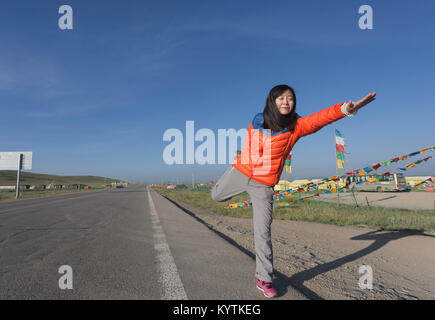 Am frühen Morgen des Plateau, eine Frau übt Yoga am Straßenrand Stockfoto