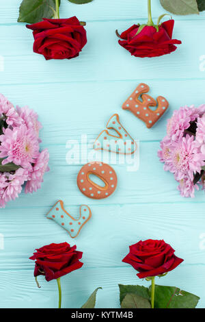 Wort Liebe in frische Blumen. Briefe der Liebe von gebackenen Plätzchen auf Blau Holz- Hintergrund, Ansicht von oben. Blumen Dekoration für Valentines Tag. Beautifu Stockfoto