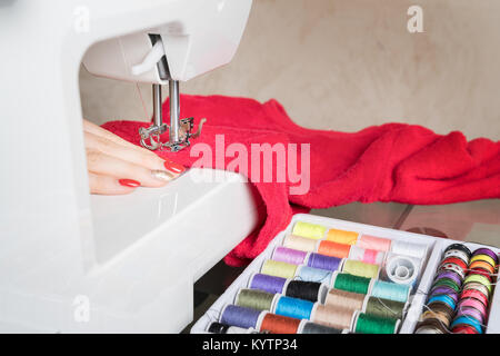 Junge Frau nähen Stoff auf der Nähmaschine, Nähen in der Phase der overstitchin, farbige Spulen. Stockfoto