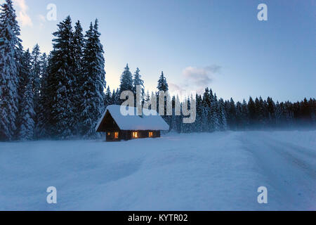 Winterlandschaft, Pinien und Cottage mit Schnee mit Leuchten in der Dämmerung, Pokljuka, Slowenien Stockfoto