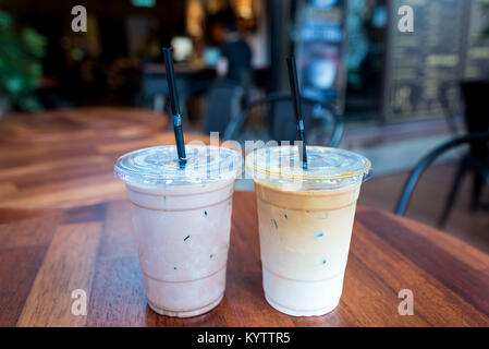 Iced Mokka und Iced Latte Kaffee Getränke in Plastikbecher mit Strohhalmen auf Holz Tisch draußen ein Cafe. Stockfoto