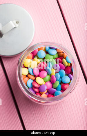 Bunte Schokolinsen in jar auf rosa Tabelle. Stockfoto