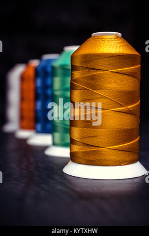 Mehrere verschiedenfarbige Spulen des Threads. Perspektive auf schwarzem Hintergrund Stockfoto