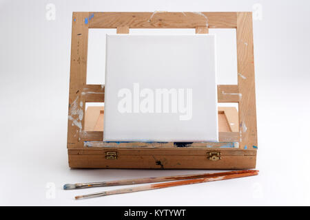 Ein Einsatz des Künstlers tragbare Staffelei und Fall auf Weiß nahtlose mit einem quadratischen leere Leinwand und zwei Bürsten warten auf ein Kunstwerk zu starten Stockfoto
