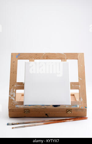 Ein Einsatz des Künstlers tragbare Staffelei und Fall auf Weiß nahtlose mit einem quadratischen leere Leinwand und zwei Bürsten warten auf ein Kunstwerk zu starten Stockfoto