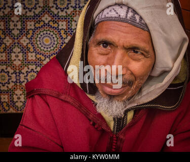Porträt einer freundlicher älterer Mann in die Kamera in eine Tür in der Medina, Marrakesch, Marokko sitzen. Stockfoto