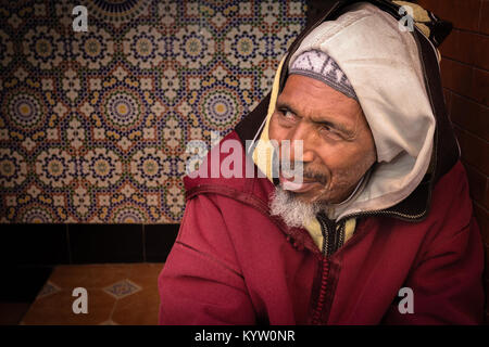 Porträt einer freundlicher älterer Mann von der Kamera weg suchen, in einem Türrahmen in der Medina, Marrakesch, Marokko sitzen. Stockfoto