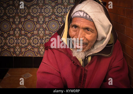 Porträt einer freundlicher älterer Mann in die Kamera in eine Tür in der Medina, Marrakesch, Marokko sitzen. Stockfoto