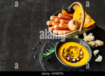 Pikante Kürbis und Karotte-Suppe mit Ingwer, Knoblauch, Zwiebel und Chili auf dunklem Hintergrund Die Suppe mit Kürbiskernöl und Croutons serviert. Platz für Ihre Stockfoto