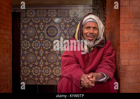 Porträt einer freundlicher älterer Mann in die Kamera in eine Tür in der Medina, Marrakesch, Marokko sitzen. Stockfoto