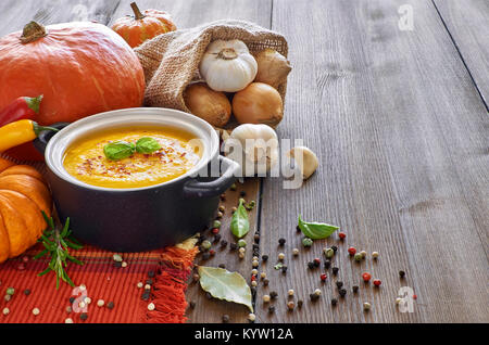 Pikante Kürbis creme Suppe mit Knoblauch, Zwiebel, Chili und Ingwer. Die Suppen in Keramik serviert pan mit Basilikum und trocken paprica auf hölzernen Tisch. Stockfoto