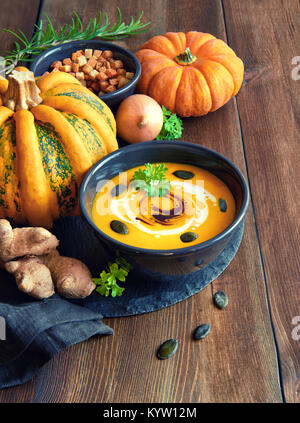 Pikante Kürbiscremesuppe mit Ingwer und Zwiebel, in schwarz Schüssel mit Kürbiskernöl, Sahne, Kürbiskerne und Petersilie auf dem hölzernen Tisch serviert. Das ist Deutsche Stockfoto