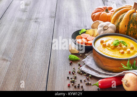 Pikante Kürbis und Karotten creme Suppe mit Knoblauch, Zwiebel, Chili und Ingwer. Die Suppen in Keramik serviert pan mit Basilikum und trocken paprica auf hölzernen Tabl Stockfoto