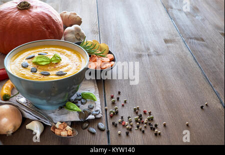 Pikante Kürbis creme Suppe mit Knoblauch, Zwiebel, Chili und Ingwer. Die Suppen in Keramik Schüssel mit Basilikum und Kürbiskerne auf hölzernen Tisch serviert. Text Stockfoto