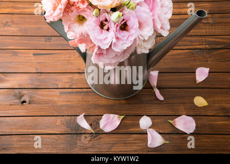 Hohe Betrachtungswinkel und der schöne zarte Blumen in Gießkanne und rosa Blütenblätter auf Holz- Oberfläche Stockfoto