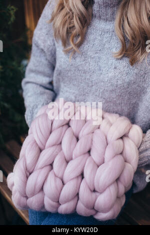 Blonde Frau im grauen pullover hält Smoky rosa gestrickt infinity Schal Stockfoto