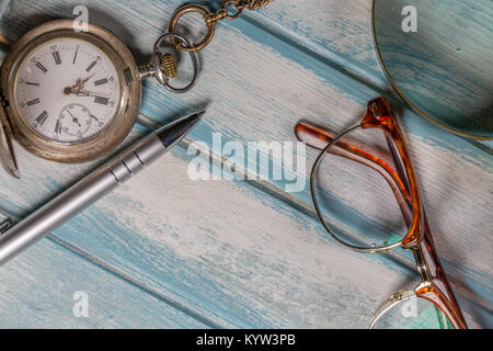 Brillen, Kugelschreiber, Silber Taschenuhr und Lupe auf Holz Stockfoto