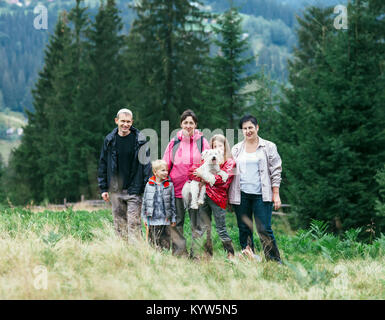 Portrait von Happy Family gegen Baum Hintergrund im Freien. Fünf Familienmitgliedern und zwei Hunde sind auf einem grünen Rasen fotografiert, hinter der wunderschönen Natur Stockfoto