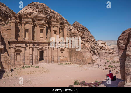 Ein Tourist im Schatten eines Felsen sitzt, beobachtet das Kloster der Stadt Petra in Jordanien Stockfoto
