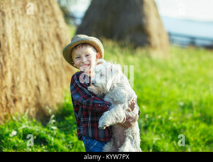 Junge umfasst stehend mit Hund, halbe Größe portrait Outdoor, Heuhaufen Hintergrund. Junge Menschen und Tiere freuen sich über die grüne Landschaft. Starke Freunde Stockfoto