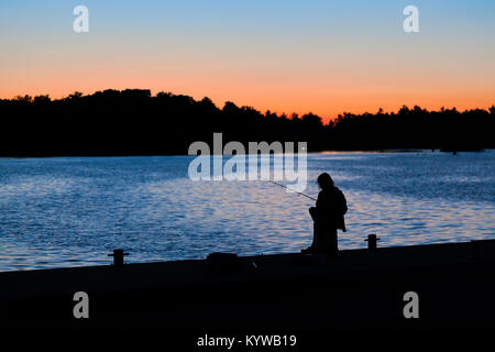 Die Silhouette eines Mädchens Angeln auf einem Pier bei Sonnenuntergang in Port Severn, Ontario, Kanada. Stockfoto