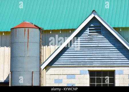 Farm Architektur hautnah mit einem kleinen Silo. Das Dach scheint neu zu sein, während das Gebäude in einem schlechten Zustand ist. Stockfoto