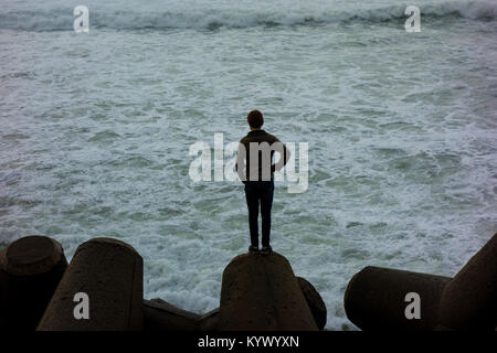 Ein Jugendlicher zu Ozean auf der Suche von einem Top Rock Stockfoto