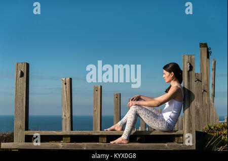 Frau sitzt auf der hölzernen Stufen am Meer, Denken und Entspannen in der Sonne ein. Stockfoto