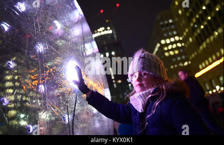 Ein Mädchen berührt die Sonic, leichte Noppen, eine Installation an der Canary Wharf Winter Lights Festival präsentiert, wie Skulpturen, Strukturen und Installationen in verschiedenen Formen der Light Technology präsentiert werden. Stockfoto