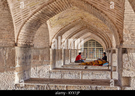 Isfahan, Iran - 24. April 2017: Bogenförmige Gewölbe der Backstein in die lange Passage unter der Brücke Khaju, Menschen ruhen, die auf die Elemente der Architektur Stockfoto