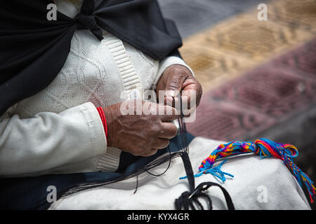 Otavalo, Ecuador - 30. Dezember 2017: Detailansicht der Hände eine indigene Frau arbeitet auf einer Artisan geknotet Souvenir auf dem lokalen Markt Stockfoto