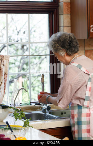 Die alte Frau ist das Waschen von Gemüse in der Küche Stockfoto