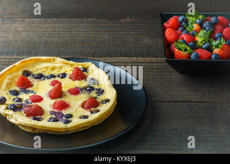 Frische hausgemachte Niederländische baby Pfannkuchen mit Heidelbeeren Himbeere und Erdbeere auf einer Platte auf einem Tisch Stockfoto