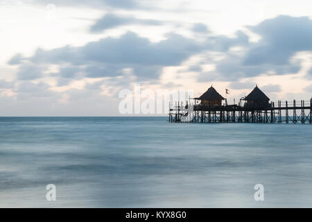 Hölzerne Seebrücke und Strohdächern an einem tropischen Strand bei Sonnenaufgang, Insel Sansibar Stockfoto