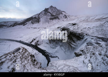 Der 62 Meter hohe Wasserfall Skogafoss im südlichen Island mit dem Drangshlidartindur Berg im Hintergrund als Menschen am unteren bewundern Sie die Teil eingefroren fällt. Stockfoto