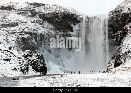 Der 62 Meter hohe Wasserfall Skogafoss im südlichen Island als Menschen bewundern die Teil eingefroren fällt. Stockfoto