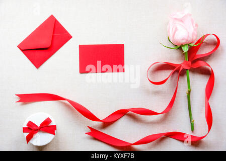 Geburtstagskarte mit einem netten Geschenk Box, einem Rosa mit roter Schleife und Schleife gebunden Rose, einen Umschlag und eine leere Nachricht Karte, auf einem vintage Stoff Hintergrund. Stockfoto