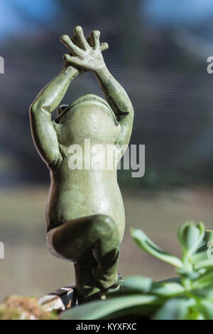 Yoga Frosch in die Baumhaltung. Figur Statue mit saftigen Haus im sonnigen Fenster. niedlich Grün kleine Objekt mit den Händen in der Luft lächelnd. Soft Focus. Stockfoto