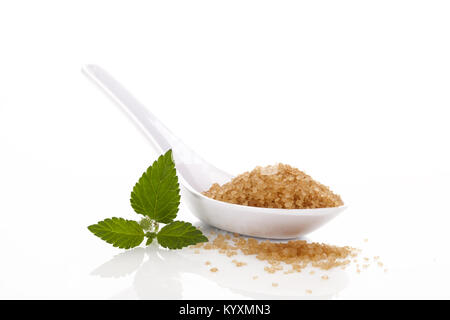 Haufen brauner Rohrzucker kristallisierte Zucker in Weiß Löffel auf weißem Hintergrund. Mit aztec Sweet herb Blatt. Stockfoto