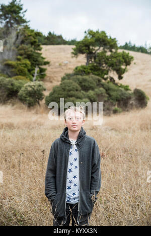 Portrait von zuversichtlich Junge mit Händen in den Taschen tragen Kapuzenjacke beim Stehen auf Feld am Park Stockfoto