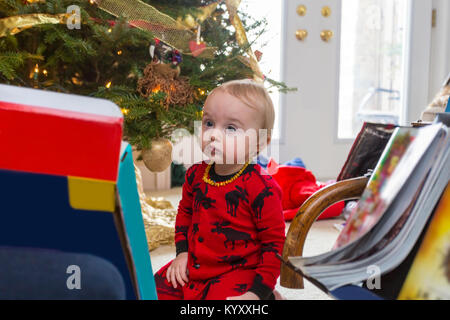 Traurig 1 Jahre alten Kind in roten Schlafanzug sitzen auf dem Boden, neben dem Weihnachtsbaum Stockfoto